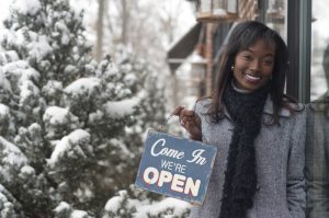 black-woman-stands-outside-retail-shop-with-sign-that-says-open